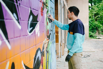Young man graffiti artist painting on the wall