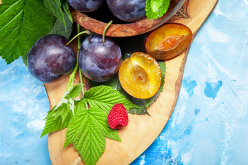Closeup still life of plums and red raspberry with green leaves on wooden dish, summer autumn fall harvest