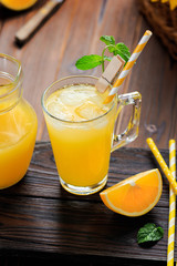Glass of fresh pressed orange juice with ice cubes and oranges on wooden table. Autumn cozy rustic mood still life