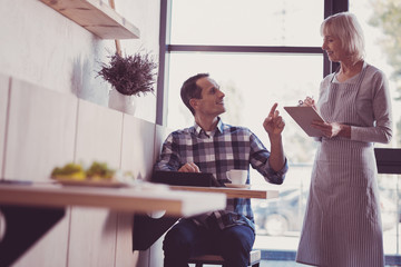 Give me an advice. Pleasant satisfied handsome man sitting by the table lifting hand and asking a...