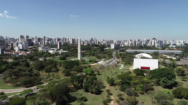 Aerial view of Ibirapuera park in Sao Paulo city, obelisk monument. Prevervetion area with trees and green area of Ibirapuera park. Office buildings and apartments in the background on a sunny day.