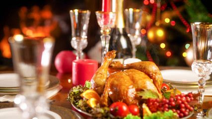 Closeup photo of hot baked chicken on festive table against Christmas tree and fireplace