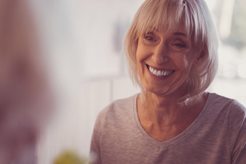 Just smile. Happy cute aged woman spending time in the bright room looking aside and smiling.