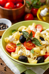 Fototapeta na wymiar Pasta salad with cherry tomatoes, black olives, feta cheese and basil on wooden background