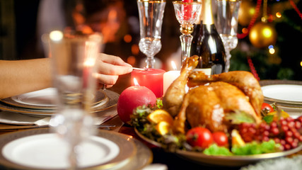 Closeup photo of lighting up candles on Christmas dinner table against burning fireplace