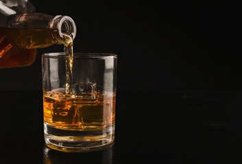 Pouring whiskey from bottle into glass with ice