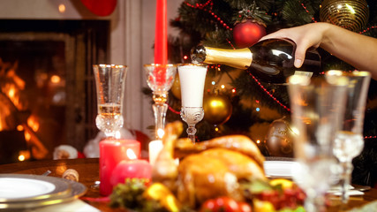 Closeup image of glasses being filled with champagne from bottle on family Christmas dinner