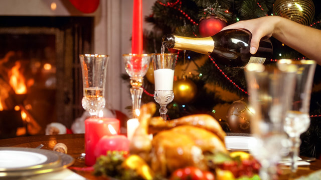 Closeup image of hand filling glasses with champagne on Christmas dining table