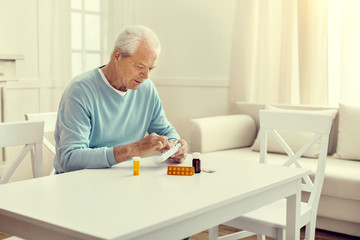 Regular intake. Waist up shot of a senior gentleman sitting at a table and opening a medication organizer before taking his pills.