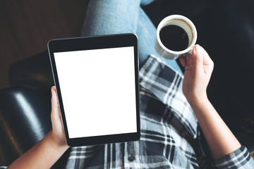 Top view mockup image of a woman sitting cross legged and holding black tablet pc with blank white desktop screen in cafe