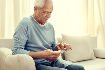 My prescription. Focused retired man sitting on a sofa and looking at a pill organizer in his hands...