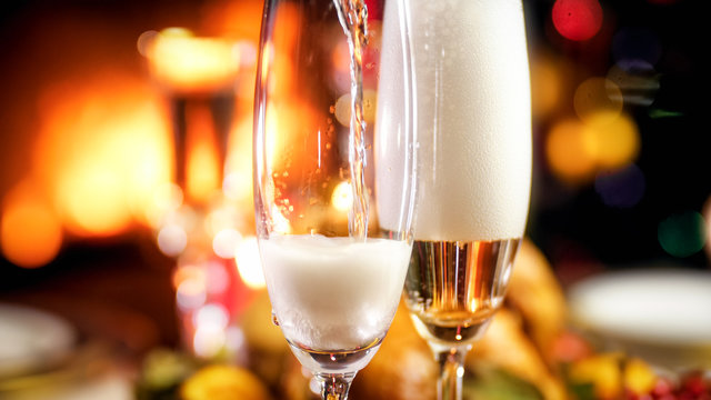 Closeup image of champagne flowing in glasses on romantic dinner at fireplace