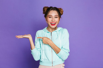 Image of young woman with two buns smiling and pointing finger at copyspace holding at palm,...