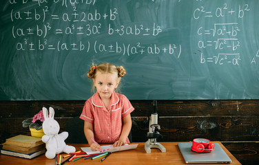 Girl drawing on chalkboard background. Little girl at teacher desk in school class. An art infused school