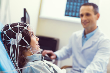 I am not afraid. Selective focus on a young lady smiling cheerfully while sitting in a lab and getting her brain analyzed during an electroencephalograph procedure.