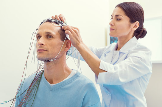 Finishing touches. Female laboratory worker fixing electrodes before examining her male patient brain on an electroencephalography machine.