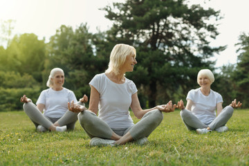 How do you feel. Cheerful ladies talking and smiling while sitting on fitness mats and practicing yoga in a local park.
