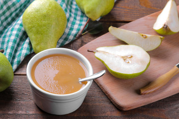 Puree with pears with fresh pears in the background on a brown wooden table