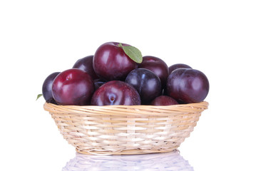 fresh ripe delicious plums in a wicker basket on a white isolated background