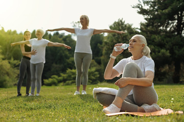 Feeling healthier. Joyful woman relaxing on a mat and drinking water after taking part in a group...