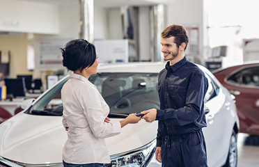Car service center scene. The mechanic giving car key to the client