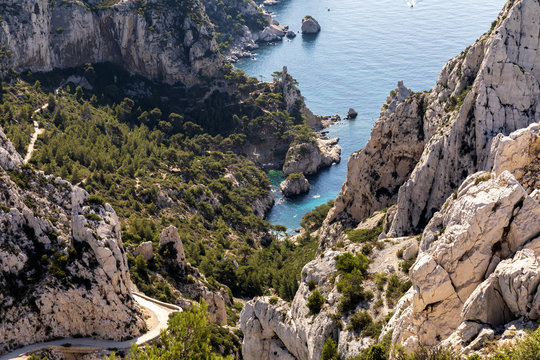 Aerial view of rocky mountains, winding road and calm sea harbour in Calanques de Marseille (Massif des Calanques), Provence, France