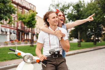 Cheerful young lovely couple posing together with retro scooter