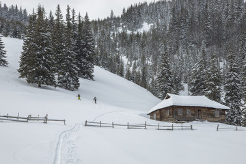 wooden house in the winter snowy Carpathian mountains. a mountainous winter landscape with a wooden house and two tourists