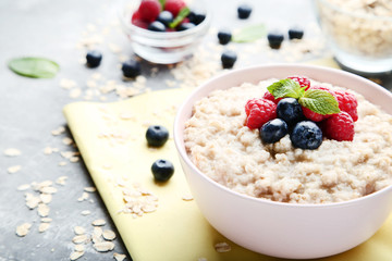Oatmeal with berries in bowl on grey wooden table