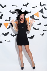 Young woman in halloween costume and paper bats on white background