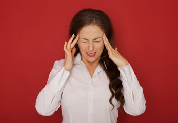 A businesswoman with a headache holding head, isolated on red background