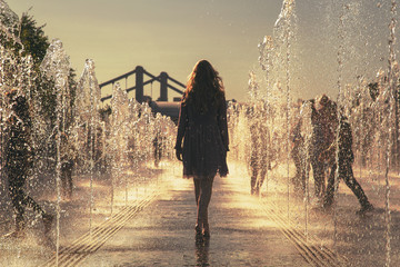 the girl in a pink dress dances among the fountains at hot summer day in a city