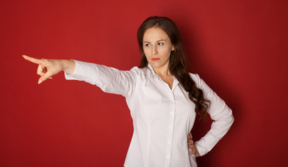 portrait of angry woman in formal wear pointing finger at something. isolated on red background