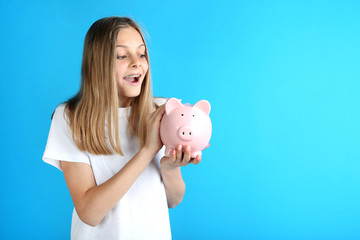 Young girl with piggy bank on blue background