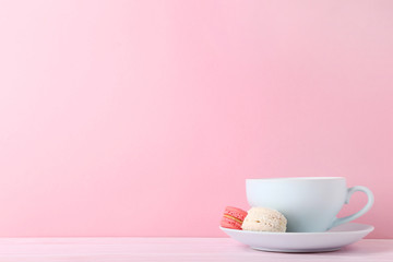 Cup of coffee with sweet macarons on pink background