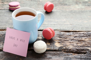 Cup of tea with sweet macarons on grey wooden table