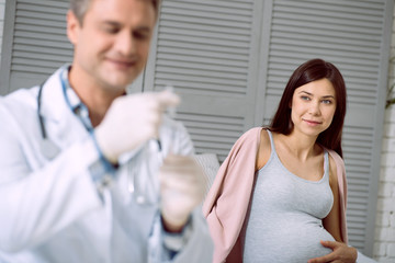 Healthcare system. Delighted nice pregnant woman smiling and looking at her doctor while visiting a hospital