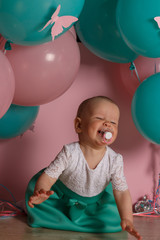 Fototapeta na wymiar little girl in blue and white dress next to balloons, smiling, holiday, year, birthday child. sits on the floor a vortex of a pacifier
