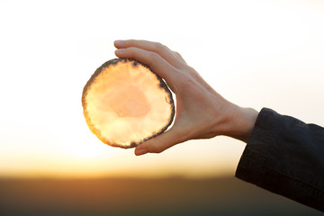 Beautiful woman hands holding agate slice crystal in the sunlight, healing crystal concept shoot,...