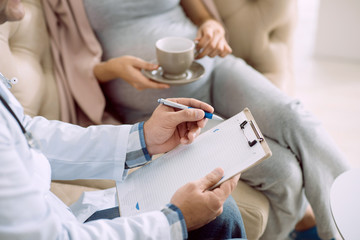 Medical treatment. Close up of notes being in doctors hands during a medical consultation with a pregnant woman