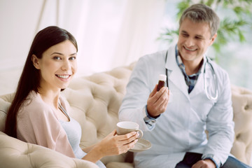 Family therapist. Cheerful positive beautiful woman having tea and looking at you while visiting her doctor