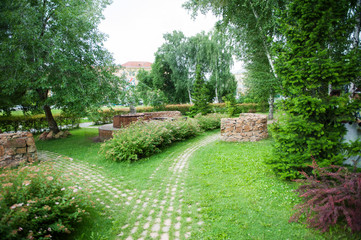 Beautiful summer park bushes, trees and flowers road lined with stone