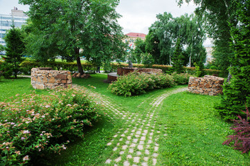 Beautiful summer park bushes, trees and flowers road lined with stone