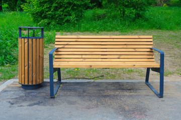 Wooden bench with metal legs and trash can in the park on a green lawn background