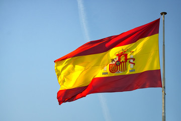 flag of spain on a mast, waving in the wind on a blue sky
