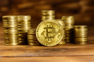Golden bitcoin and stacks of coins on wooden background