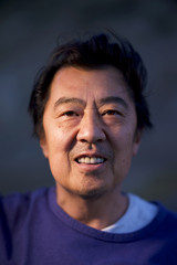 Portrait of a middle age asian man, smiling under the dusk light. Mature man closeup smiling.