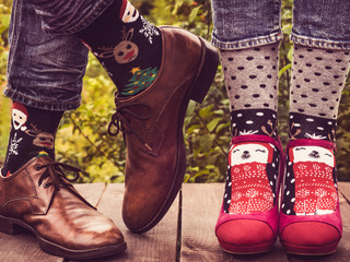 Female and male legs in stylish shoes, bright, colorful socks with a Christmas and New Year pattern on the background of trees. Lifestyle, fashion, fun