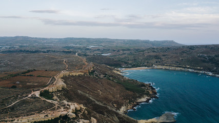 Obraz premium Aerial drone view of bay with clear blue water and shore with cliffs. Sunset, dusk. Mediterranean sea. Malta
