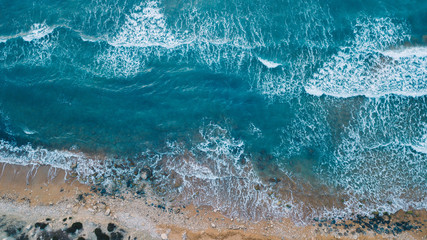 Scenic aerial view of turquoise sea water with waves and white foam hitting the sea shore with white sand. Summer vacation concept. Mediterranean sea. Malta. Golden Bay